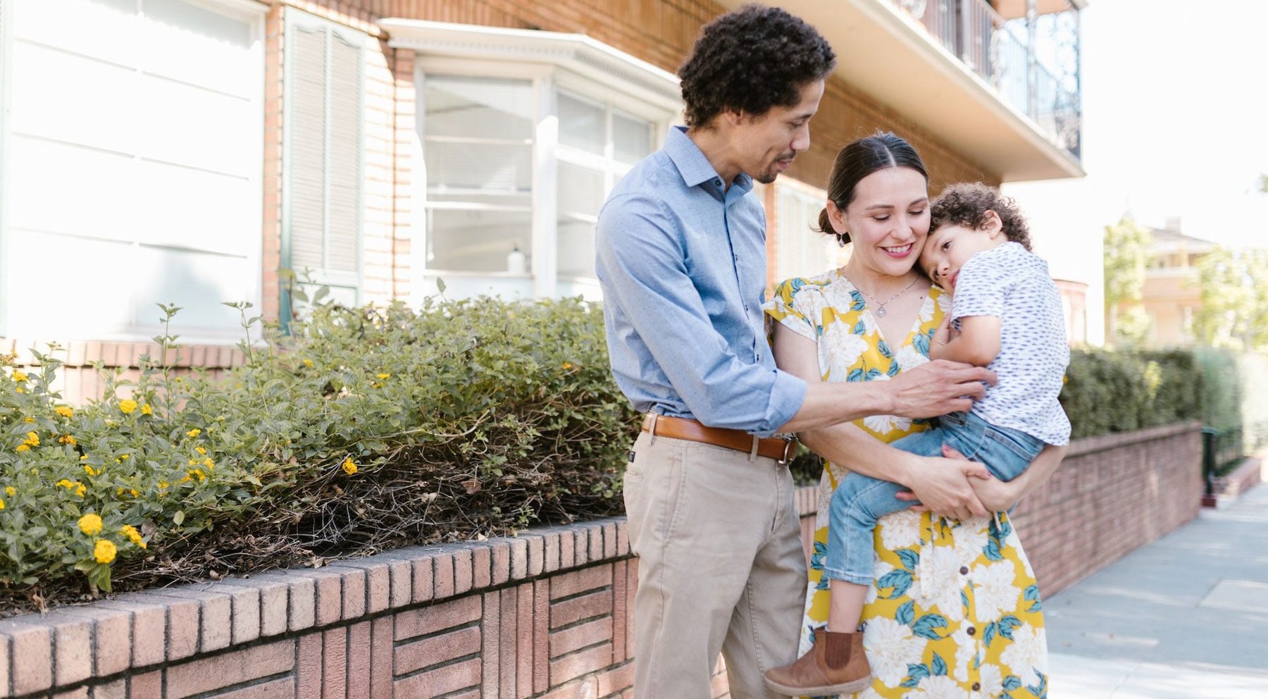 A father and mother holding their young child outside their home